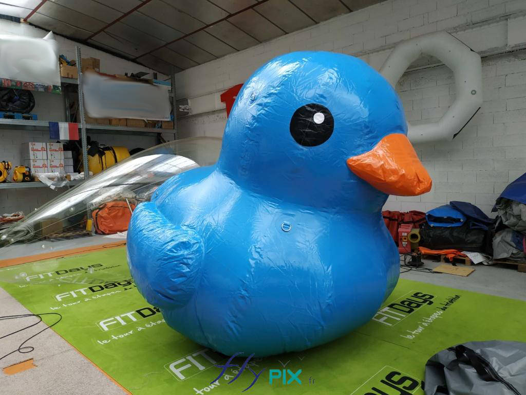 Ballon gonflable mascotte canard géant, de couleur bleu, air captif, en enveloppe PVC, avec un bec jaune.