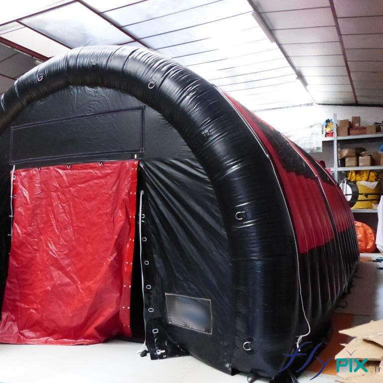 Tente gonflable en forme de tunnel de couleur noire, pour le stockage de matériel pendant des longues durées en extérieur: porte large pignon de couleur rouge.