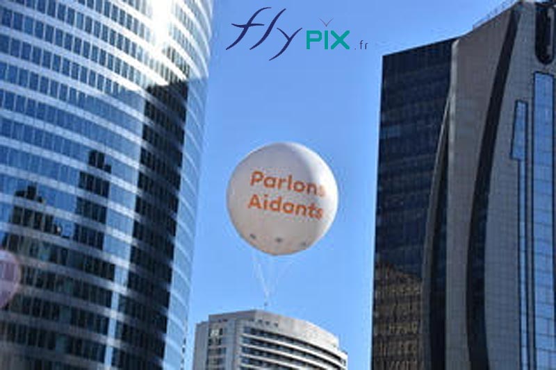 Un ballon publicitaire sphérique D = 2.5 m, gonflé à l'hélium, survole la Place de la Défense à Paris.