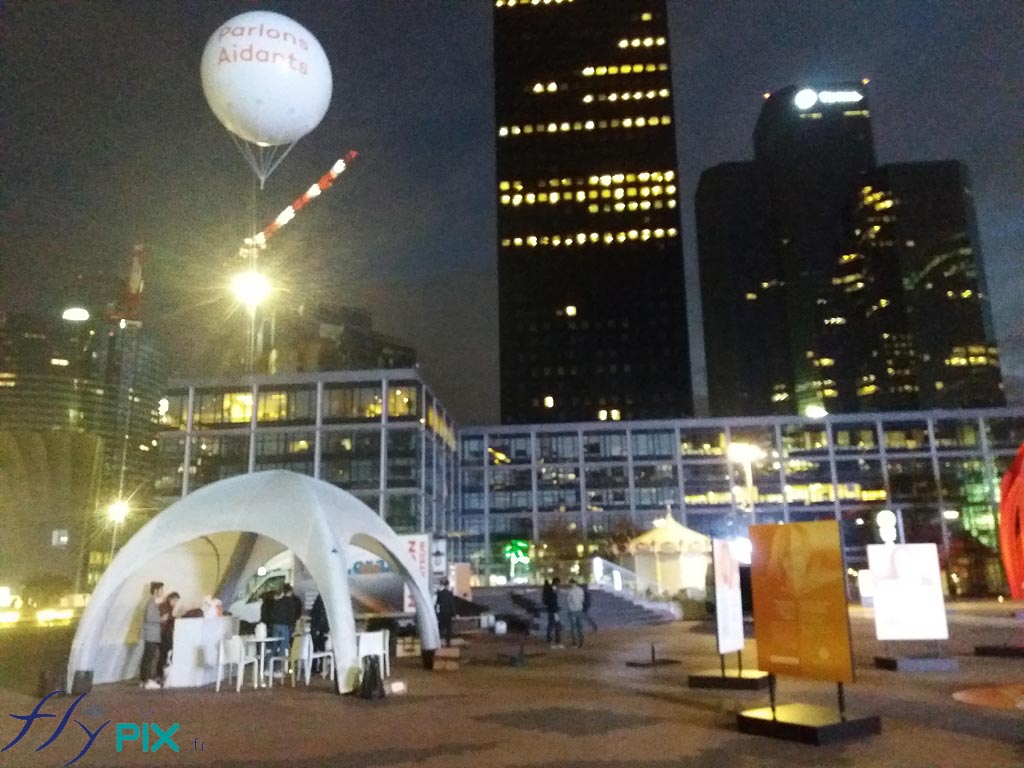 Une vue de nuit montre le ballon publicitaire à hélium, en forme de sphère et imprimé de marquages personnalisés en couleur sur fond blanc.